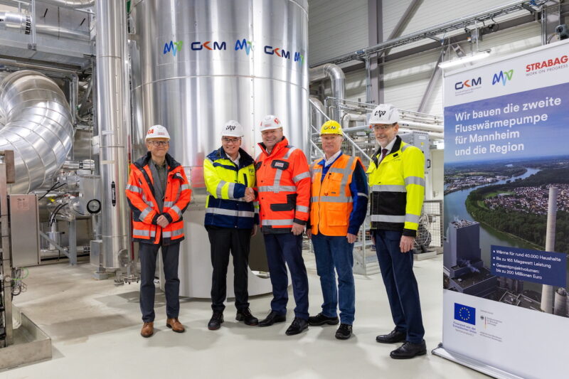 Die fünf Verantwortlichen stehen vor einem Stahltank in der Flusswärmepumpen-Anlage Mannheim.