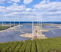 Das Bild zeigt das Photovoltaik-Projekt Energiepark Lausitz in einer Luftaufnahme. Neben und zwischen den Solar-Feldern stehen Windkraft-Anlagen