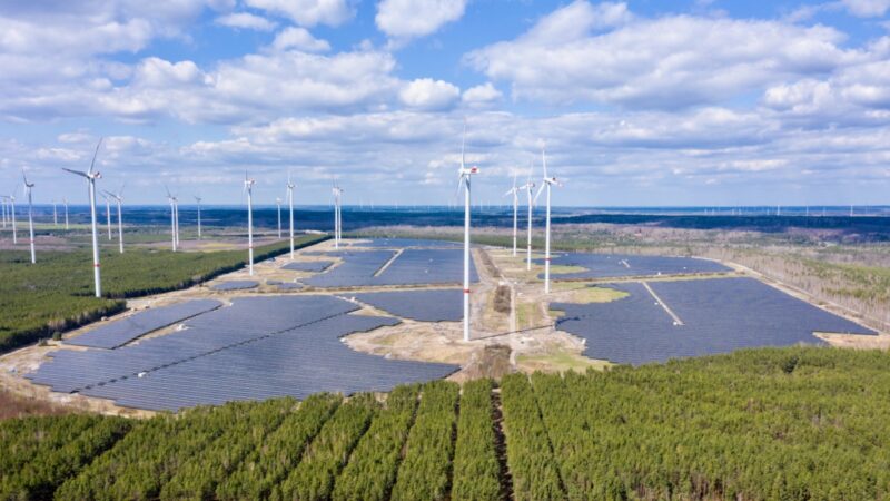 Das Bild zeigt das Photovoltaik-Projekt Energiepark Lausitz in einer Luftaufnahme. Neben und zwischen den Solar-Feldern stehen Windkraft-Anlagen