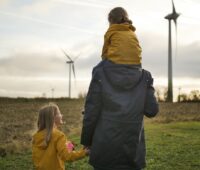 Zu sehen ist eine Person mit zwei Kindern vor einem Windpark als Symbol für GP Joule Invest Crowd.