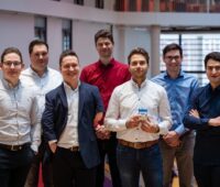 Sieben junge Männer im legeren Business-Outfit im Büroumfeld.