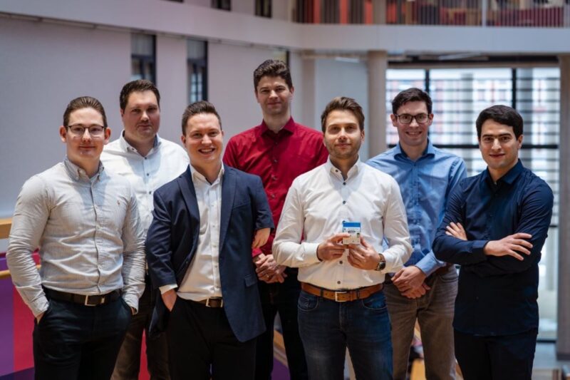 Sieben junge Männer im legeren Business-Outfit im Büroumfeld.