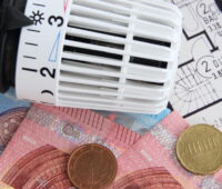 Das Foto zeig in Draufsicht einen Wohnungsgrundriss, Banknoten 50er, 20er, 10er sowie Münzen neben einem Heizungsthermosthat.