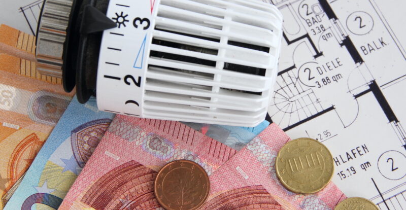 Das Foto zeig in Draufsicht einen Wohnungsgrundriss, Banknoten 50er, 20er, 10er sowie Münzen neben einem Heizungsthermosthat.