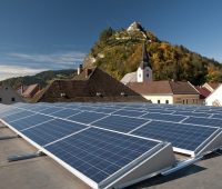 Foto einer PV-Anlage auf einem Flachdach. Im Hintergrund ein Österreichisches Dorf und Berge.