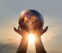 Eine Erdkugel von zwei Händen gehalten vor der Sonne - Symbol für Energiewende weltweit.