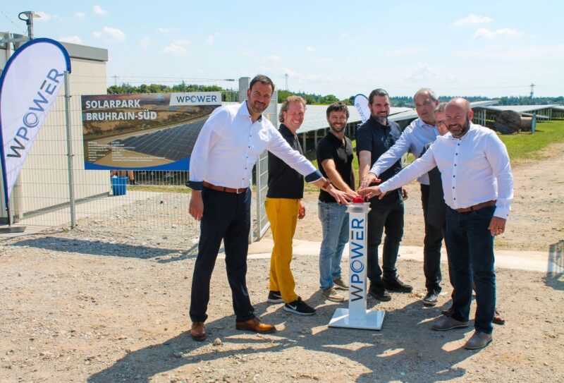 Sechs Personen geben symbolischen Startschuss für einen Solarpark im HIntergrund.