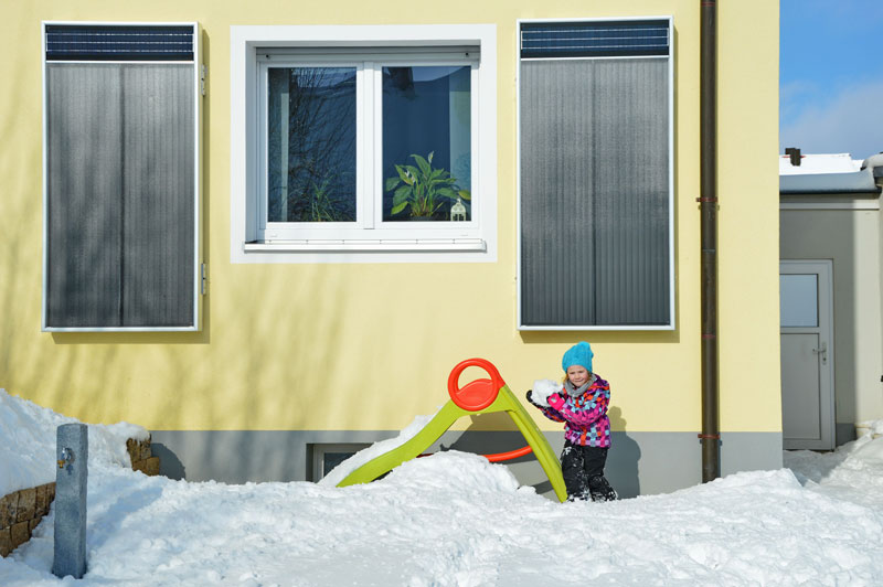 zwei Solar-Luftkollektoren an der Fassade eines Wohnhauses mit spielendem Kind um Schnee