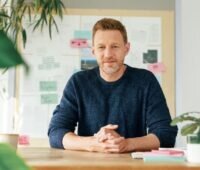 Nils Müller sitzt an einem Holzschreibtisch in einem Büro.