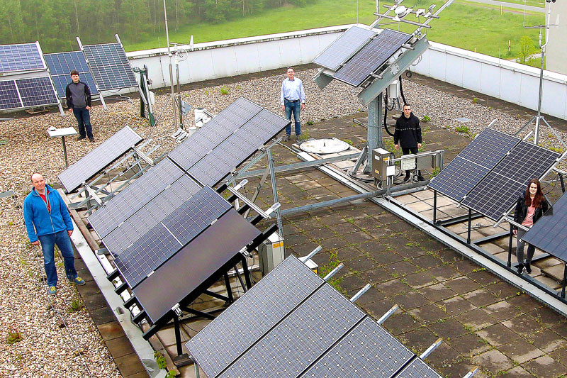 Fünf Mitarbeiter:innen präsentieren Photovoltaik-Teststand auf einem Dach der Hochschule Gelsenkirchen, wo auch bifaziale PV-Module getestet werden.