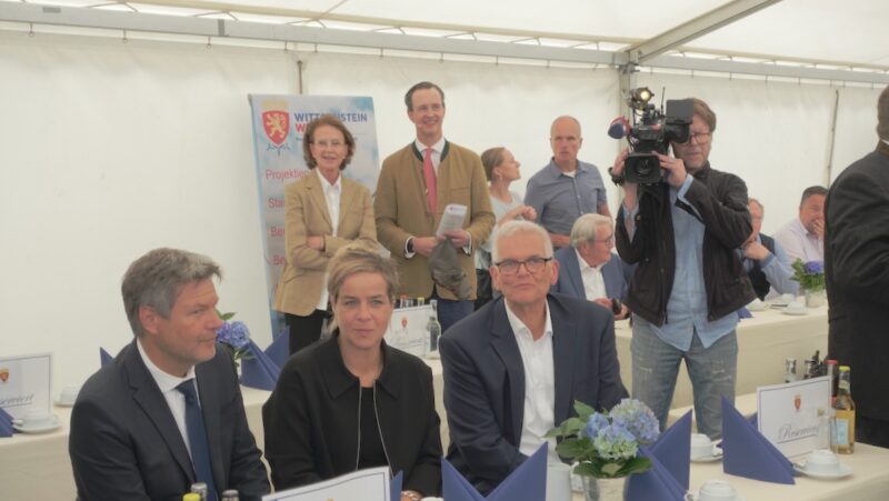 Drei Menschen (Habeck, Neubaur, Vogel) sitzen am Tisch in einem Zelt, im Hintergrund stehen zwei Menschen an der Zeltwand - Einweihung von Wald-Windpark