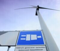 Zu sehen ist eine Windkraftanlage und ein Hinweisschild zur Landstromanlage mit Windenergie im Rotterdamer Hafen.