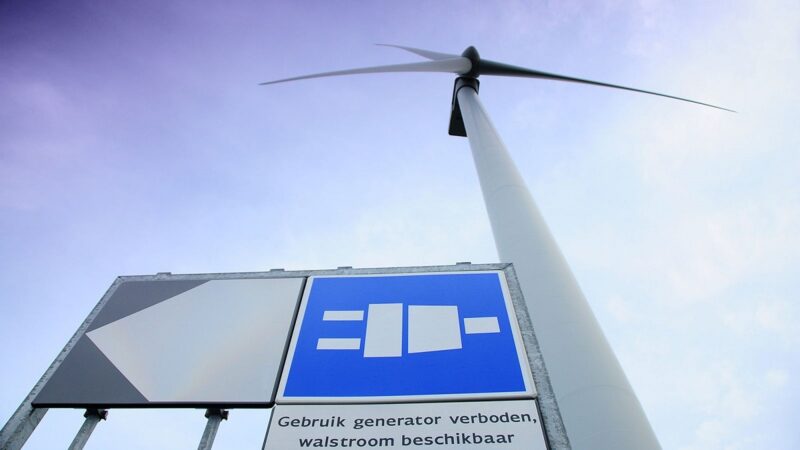 Zu sehen ist eine Windkraftanlage und ein Hinweisschild zur Landstromanlage mit Windenergie im Rotterdamer Hafen.