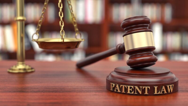 Hammer und im Hintergrund eine Waage als Symbol für den Streit um ein Patent, Patentstreit