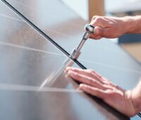 Symbolbild für Photovoltaik-Umsatzsteuer: Handwerker schraubt Modulklemmen einer Photovoltaikanlage fest.