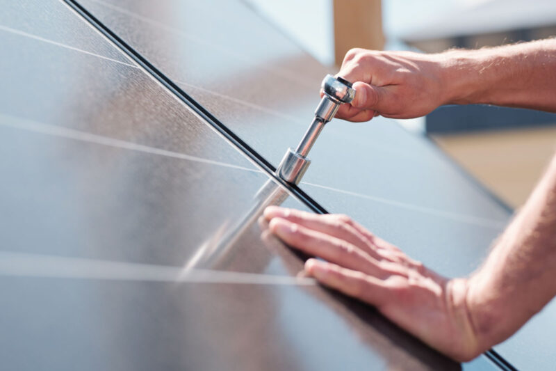 Symbolbild für Photovoltaik-Umsatzsteuer: Handwerker schraubt Modulklemmen einer Photovoltaikanlage fest.