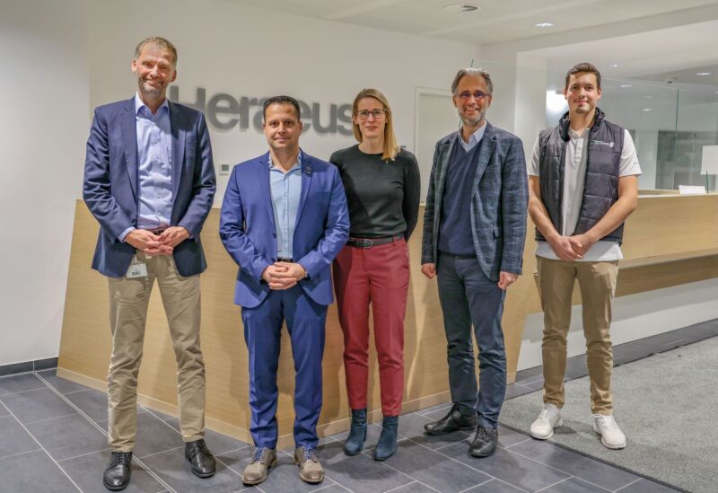 Fünf Personen der Firmen Heraeus und Next Energy in einem Bürogebäude blicken in die Kamera.