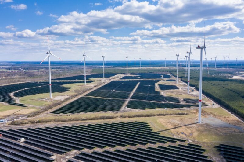 Auf einer sandigen Fläche stehen Windräder und eine große PV-Anlage.