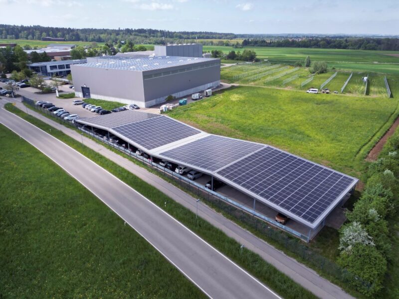 Luftbild mit wellenförmigen PV-Parkplatzdach neben Firmenzentrale
