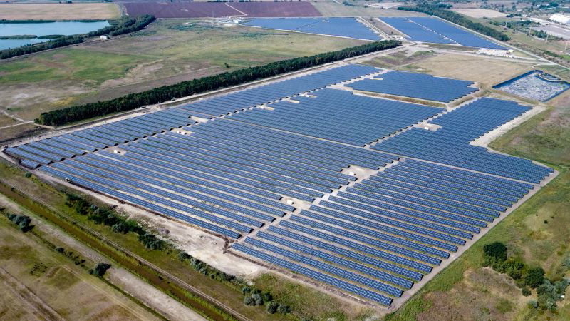 Luftbild eines großen PV-Parks auf grüner Wiese.