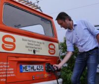 Ein Mann lädt seinen alten VW Bulli mit Strom.