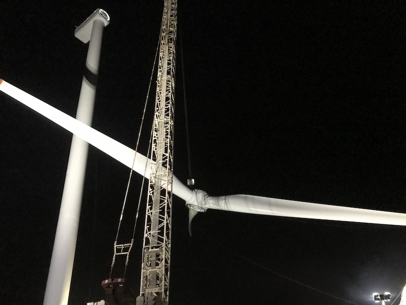 Ein Kran zieht bei Nacht den Rotor einer Windenergie-Anlage in die Höhe.