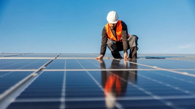 Mann mit Helm hockt auf Dach neben PV-Anlage - Symbolbild für Solardachpflicht in Nordrhein-Westfalen