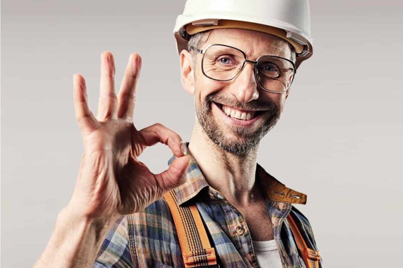 Handwerker mit weißem Bauhelm und Brille hält seine Hand mit dem OK Zeichen in die Kamara