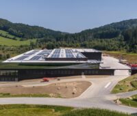 Neu gebautes Industriegebäude mit Photovoltaik auf dem Dach, umgeben von hügeliger grüner Landschaft.
