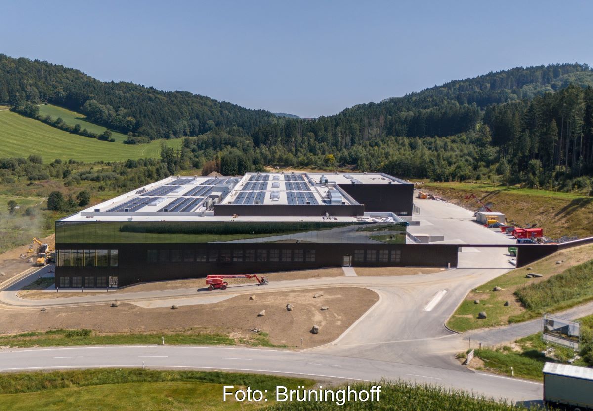 Neu gebautes Industriegebäude mit Photovoltaik auf dem Dach, umgeben von hügeliger grüner Landschaft.