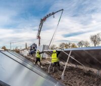 Monteure in gelben Westen installieren große Solarwärmeanlagen. Dabei hilft ein Kran, der im Hintergrund agiert.