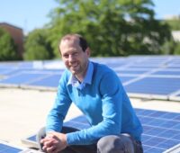 Installation-Gründer Meyer-Delpho lachend auf einem Dach mit Solarmodulen.