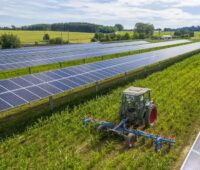 Zu sehen ist ein Mini-Traktor, der zwischen Reihen von Photovoltaik-Modulen das Land beackert.