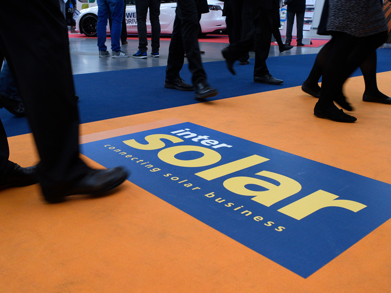 Photo mit Beinen, die über einen Teppich laufen, der mit "Intersolar connecting solar buisiness" beschriftet ist