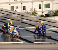 Handwerker realisiern auf einem Dach PV-Anlagen.