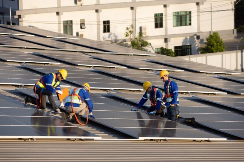 Handwerker realisiern auf einem Dach PV-Anlagen.