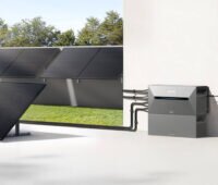 Zu sehen sind Photovoltaik Module, die an einer Garage angebracht bzw. auf einer Terasse stehen und die mit einem Anker Solix Speicher verbunden sind.