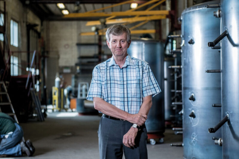 Josef Jenni in seiner Fabrik. Rechs sind zwei große Solarspeicher-Tanks zu sehen.