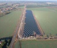 Luftbild eines Freiflächensolarparks entlang einer Bahntrasse.