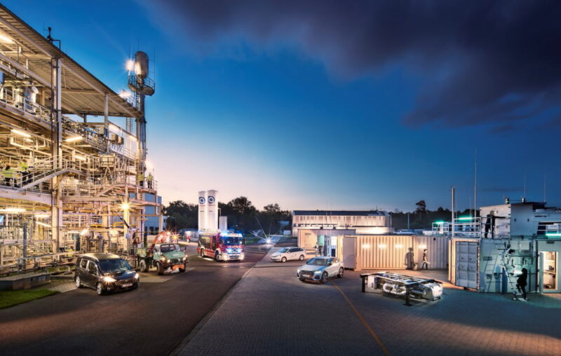 Eine Raffinerie bei spätem Sonnenuntergang mit verschiedenen Fahrzeugen sowie Menschen, die arbeiten.