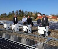 Mehere Personen freuen sich auf dem Flachdach eines Gebäudes über eine dort installierte PV-Anlage.