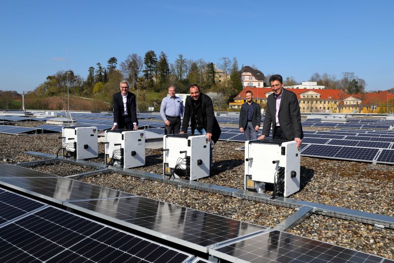 Mehere Personen freuen sich auf dem Flachdach eines Gebäudes über eine dort installierte PV-Anlage.