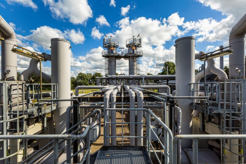 Eine Konstruktion aus grauen Pipelinen und Stangen mit zwei Männern in roter Weste im Hintergrund auf Türmen.