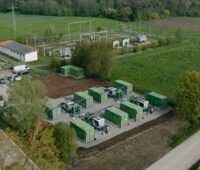Luftbild zeigt Großspeicher mit zehn Batteriecontainern auf der grünen Wiese.