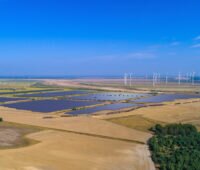Ein Solarpark zwischen braunen Landwirtsschaftsflächen und blauem Himmel aus der Vogelperspektive.