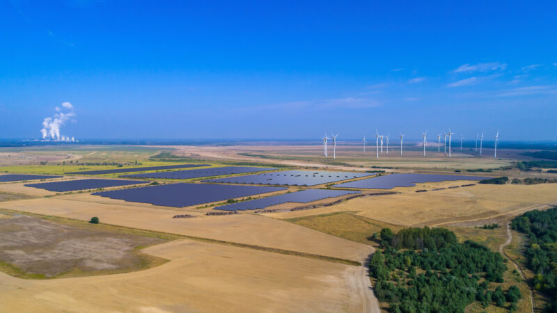 Ein Solarpark zwischen braunen Landwirtsschaftsflächen und blauem Himmel aus der Vogelperspektive.