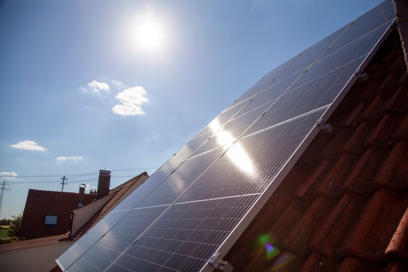 Eine Solaranlage auf Schrägdach im Gegenlicht der Sonne am Himmel.