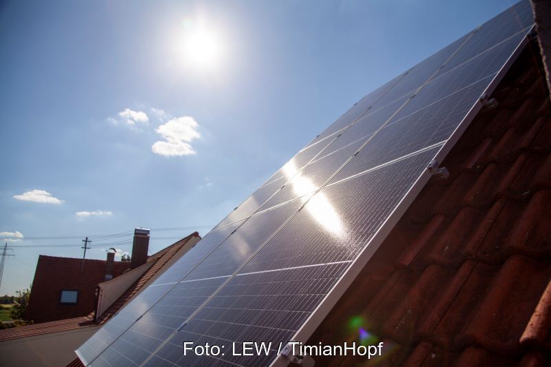 Eine Solaranlage auf Schrägdach im Gegenlicht der Sonne am Himmel.