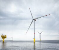 Windenergieanlagen stehen vor einem blassen Himmel im Wasser.