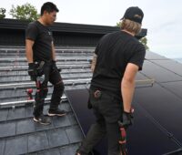 Zwei Installateure bei der Montage von Solarmodulen auf einem Schrägdach.